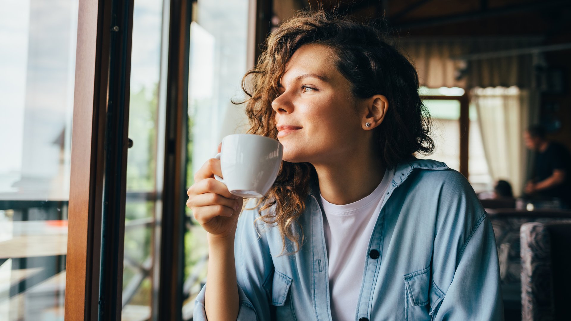 Junge ehemalige Patientin sitzt im Café und hat eine Tasse in der Hand